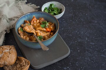Tripas - pork tripe stew with white beans and smoked sausages in a blue bowl on the dark table. Copy space