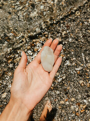Woman hand manicure holding white beautiful stones above sea sandy summer beach.