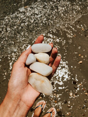 Woman hand manicure holding white beautiful stones above sea sandy summer beach.