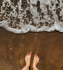 Woman legs barefoot at sea foam waves on sand beach summer day. top view above women feet.