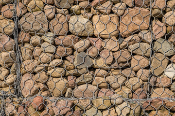 engineering structure made of stones behind metal wire netting to strengthen the river bank near the road bridge