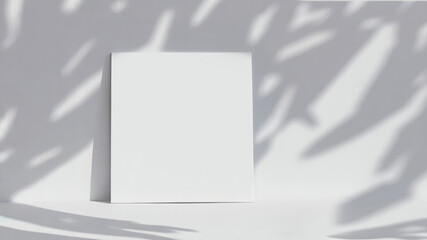 White wall with soft shadows from leaves and a square mockup standing on the floor