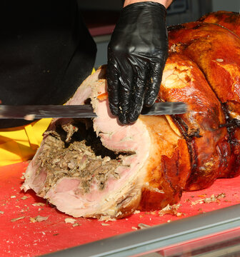 butcher with black glove cuts slices of porchetta a pork salume