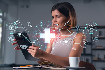 Smiling businesswoman in casual wear holding tablet device touching it at office workplace. Concept of distant work, business education, information technology. Health care icons hologram