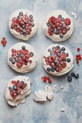 Mini Pavlova meringues with raspberries, red currant and blueberries over light blue concrete background. Top view