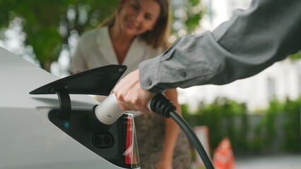Young couple travel with EV electric car charging at green sustainable home in summer shows urban...