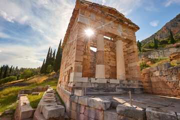 Greek history theme: Athenian Treasury ruins in Delphi against sun, low angle, ultra wide photo, sun and rays, beautiful day. UNESCO World Heritage Site, Greece.