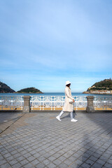 Stylish woman with white coat and hat on Paseo de la Concha