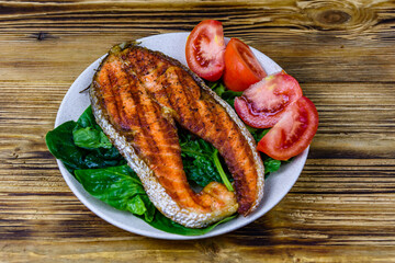 Plate with roasted salmon steak, tomtoes and spinach leaves on a wooden table