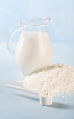 Powdered milk on a blue background with a jug of whole milk
