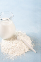Powdered milk and whole milk in a jug on a light blue background