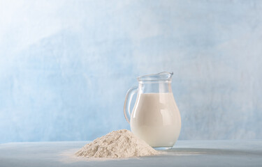 Powdered milk and whole milk in a jug on a light blue background