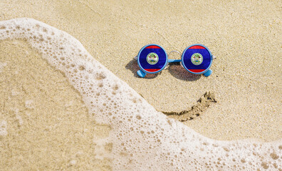 A painted smile on the sand and sunglasses with the flag of the Belize. The concept of a positive and successful holiday in the resort of Belize.