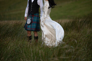 A newly married Scottish couple strolls through a grassy field in Glencoe, the Scottish highlands....