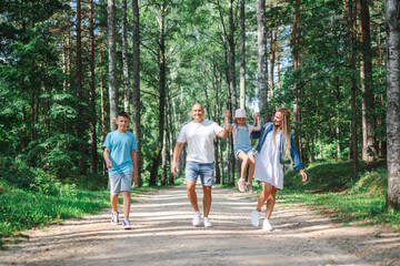 Young Family of four enjoying a walk in the forest, parents swinging the daughter, and the teenage children strolling alongside. for themes of family bonding and nature outings.