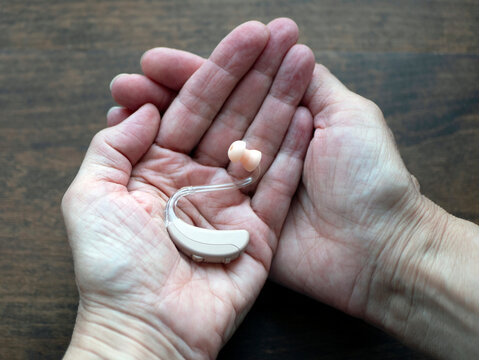 Hearing aid in hands, small electronic device that person wears behind the ear. World hearing day