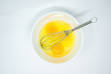 Fototapeta na wymiar Three egg yolks and egg whites in a bowl with a whisk on a white background with copy space