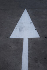 Closeup of a white arrow painted on gray asphalt indicating forward