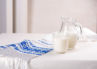 Glass and jug of milk on a light background and light blue tablecloth
