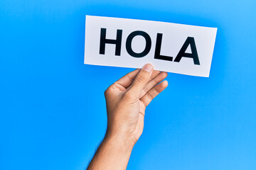 Hand of caucasian man holding paper with hola word over isolated blue background