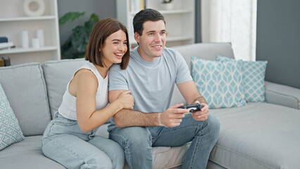 Beautiful couple playing video game sitting on sofa at home