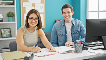 Two workers man and woman sitting on table smiling at the office