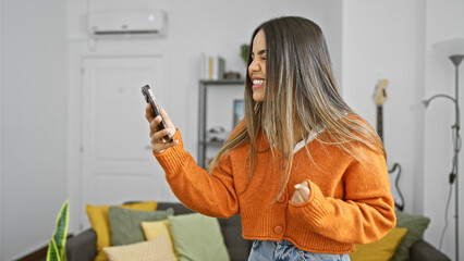 A cheerful young woman enjoying music on her phone in a modern living room