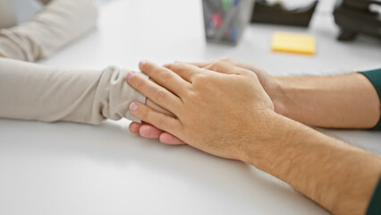 A man and woman teaming up in a bright office touching hands in a supportive gesture.