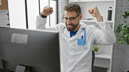 Naklejka na ściany i meble Triumphant win! young hispanic male doctor celebrates working diagnosis at the clinic, confident smile behind glasses, bearded and handsome