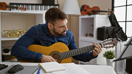 Captivating young hispanic man engrossed in playing a classic guitar melody at a music studio...