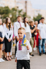 A little boy, child, Ukrainian schoolchild in an embroidered shirt walks with a flag in his hands outdoors at a school day celebration in Ukraine. Photography, portrait.