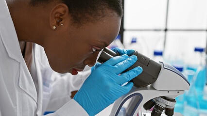Beautiful, focused african american woman scientist working meticulously with a microscope in a...