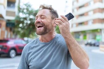 Middle age man smiling confident listening audio message by the smartphone at street