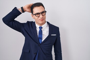 Young hispanic man wearing suit and tie confuse and wonder about question. uncertain with doubt, thinking with hand on head. pensive concept.