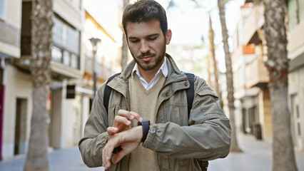 A young hispanic man with a beard checks time on his watch in an urban street setting, portraying a casual and stylish lifestyle.