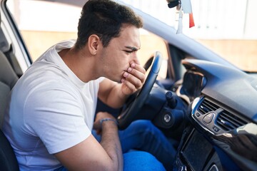 Young hispanic man smelling bad aroma sitting on car at street