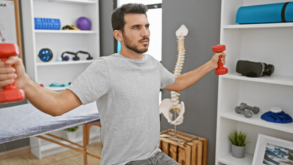 Fototapeta na wymiar A young hispanic man exercises with dumbbells in a modern physical therapy clinic's rehabilitative setting.