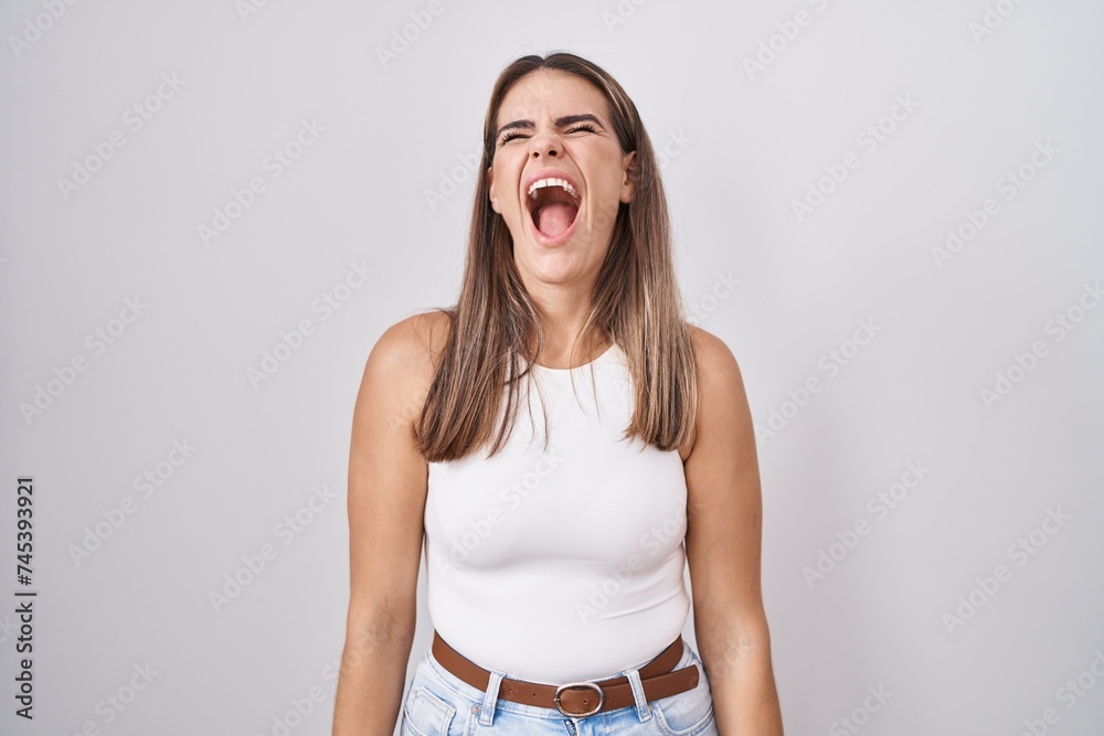 Poster hispanic young woman standing over white background angry and mad screaming frustrated and furious, 