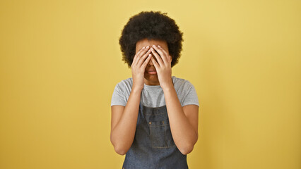 Portrait of an emotional african woman covering her eyes with her hands against a yellow background