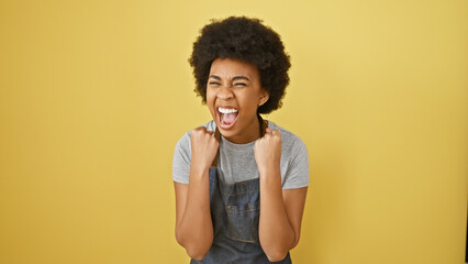 Excited african american woman with curly hair cheering against a vibrant yellow background.