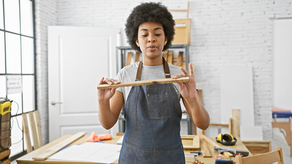 African american woman carpenter examining wood in workshop