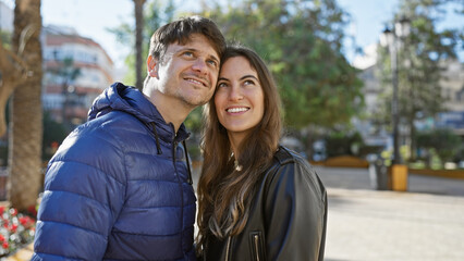 Loving couple embracing outdoors in a city park, showcasing a close relationship between a man and woman in a casual urban setting.