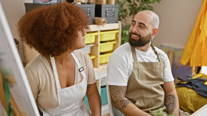 At the art studio, two smiling artists, partners in creativity, sitting together, engaging in...