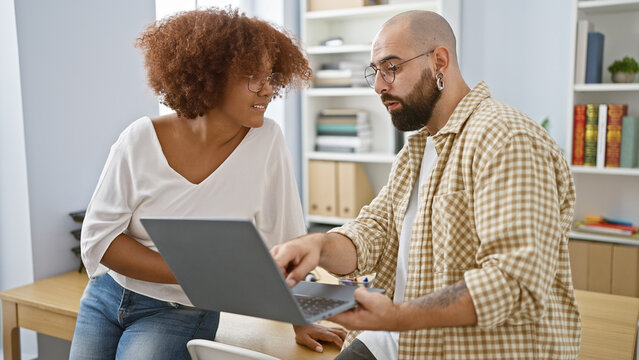 Confident man and woman partners enjoying their work at the office, smiling as they use laptop