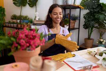 Young african american woman florist smiling confident wearing gloves at flower shop