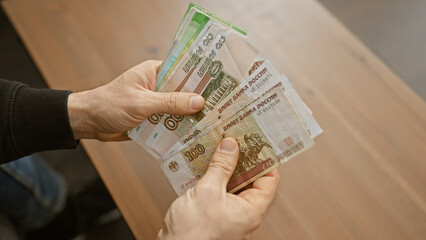 Close-up of man's hands counting russian rubles indoors, suggesting financial transactions or...