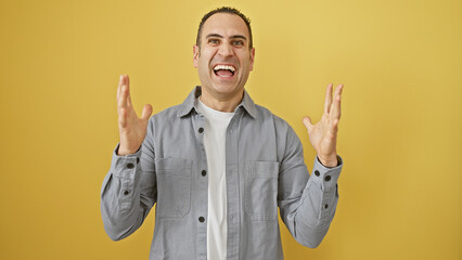 A cheerful hispanic man gesturing excitement against a vibrant yellow wall, expressing joy and happiness.