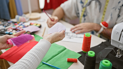 Fototapeta premium Two tailors working with fabrics and sewing accessories in a tailor shop, crafting custom garments.
