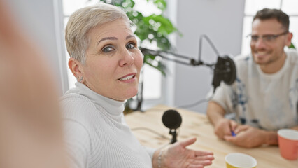 A woman talking into a microphone on a radio show with a smiling man in a studio setting