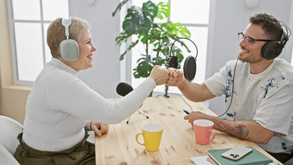 A woman and man fist-bumping with smiles in a podcast studio interior with microphones and...